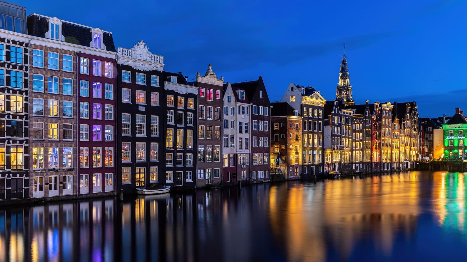 Grachtenpanden aan het Damrak in het blauwe uur, weerspiegeld in het water