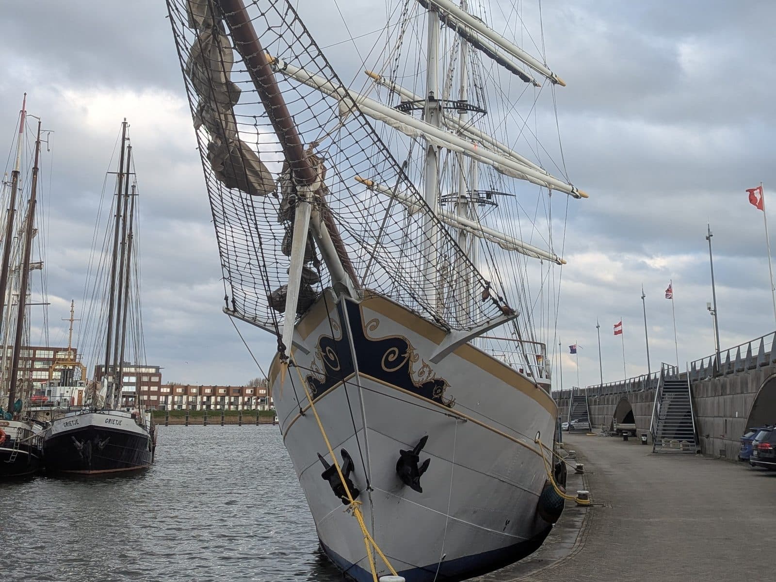 De boeg van een driemaster aan de kade van de Bataviahaven, met andere zeilschepen ernaast